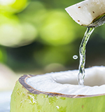 Glass of coconut water with young coconut wedges—100% pure and natural.