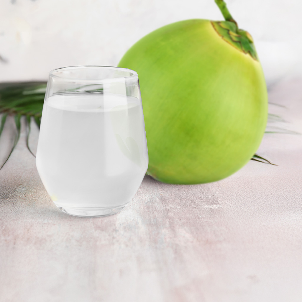 Glass of coconut water with a young green coconut behind it.